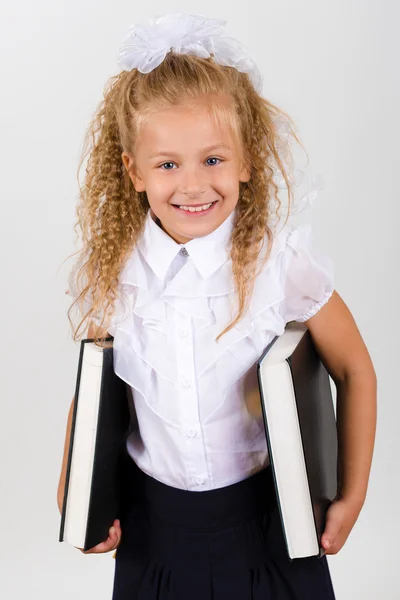 Porträt eines schönen lächelnden kleinen Mädchens in Schuluniform. Sie hält zwei große Bücher in ihren Händen — Stockfoto