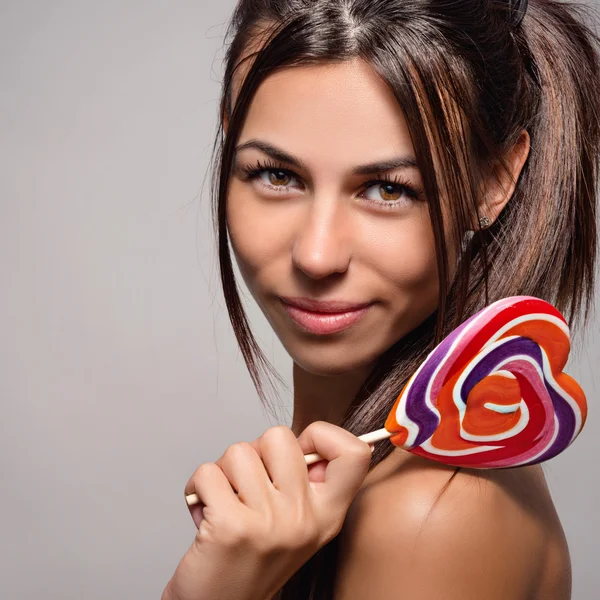 Portrait of a beautiful young woman with candy on a stick in the form of heart — Stock Photo, Image