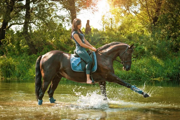 Žena na koni jezdí podél řeky na horkém letním dni. — Stock fotografie