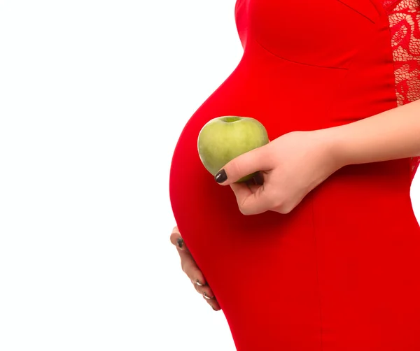 Pregnant woman holding a green apple on the background of the abdomen — Stock Photo, Image