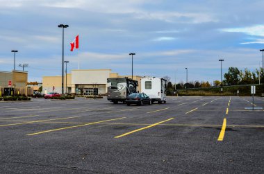 Karavanlar boş bir alışveriş merkezinin otoparkında, mavi gökyüzünde Kanada bayrağı var.