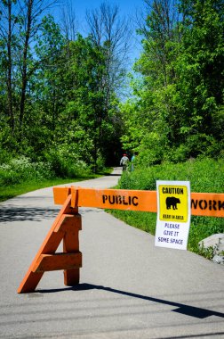Park yolunda arka planda insanların olduğu Ayı Uyarı İşareti