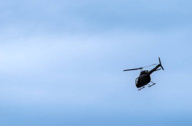 İnce bulutlu mavi gökyüzüne karşı tek bir helikopter bir açıyla uçuyor.
