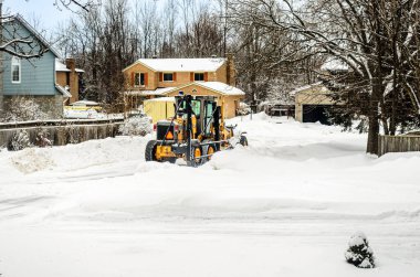 Şiddetli bir kar yağışından sonra, bir Motor Grader kar küreme aracı yerleşim alanındaki sokakları temizliyor.
