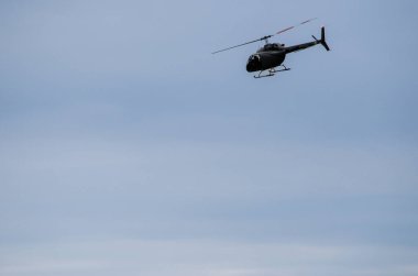 İnce bulutlu mavi gökyüzüne karşı tek bir helikopter bir açıyla uçuyor.