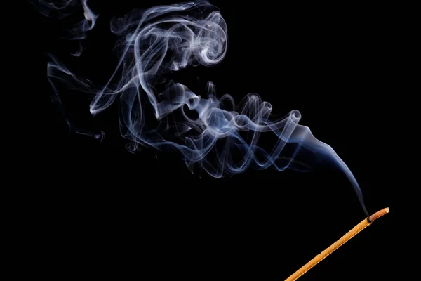 Burning incense stick and smoke isolated on a black background. Copy space.