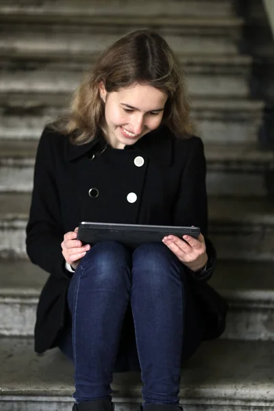 Girişteki basamaklarda oturan kız blogcu tablet ya da dizüstü bilgisayar kullanıyor