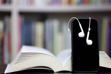 Kitap, telefon ve kulaklıklar bulanık kitaplık arka plan, okuma ve öğrenme