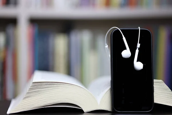 Kitap, telefon ve kulaklıklar bulanık kitaplık arka plan, okuma ve öğrenme
