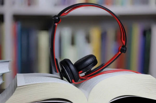 book and headphones on blurred bookshelf background, reading and learning