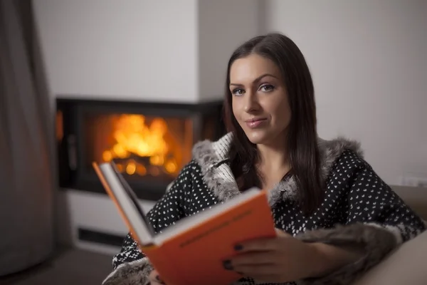 Portrait of beautiful woman reading book by fireplace — Stock Photo, Image