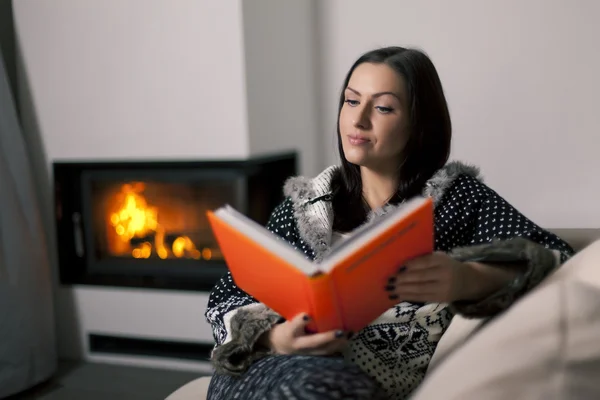 Portrait of beautiful woman reading book by fireplace — Stock Photo, Image