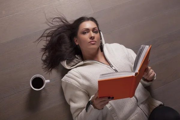 Beautiful woman lying on floor and reading book by fireplace and — Stock Photo, Image