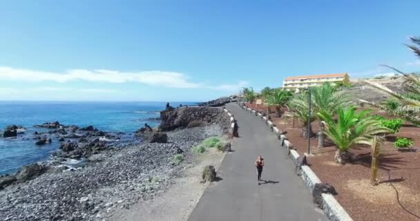 Beautiful smooth areal shot of young white woman jogging along the North Atlantic ocean coast. Playa San Juan, Tenerife island, Spain — Stock Video