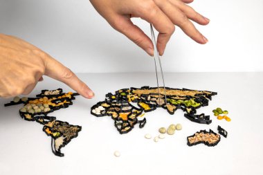 A hand with tweezers rearranging a world map made of various food ingredients and spices clipart
