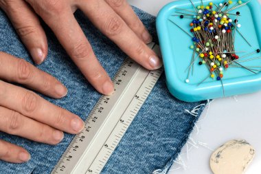  Bir tarafında iğne ve terzi tebeşiri olan kot pantolon kumaşı üzerine cetvel tutan iki el.