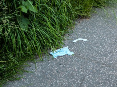 Kullanılmış, parçalanmış ve kirli yüz maskesi beton zeminde çimen ve otlarla büyümüş.