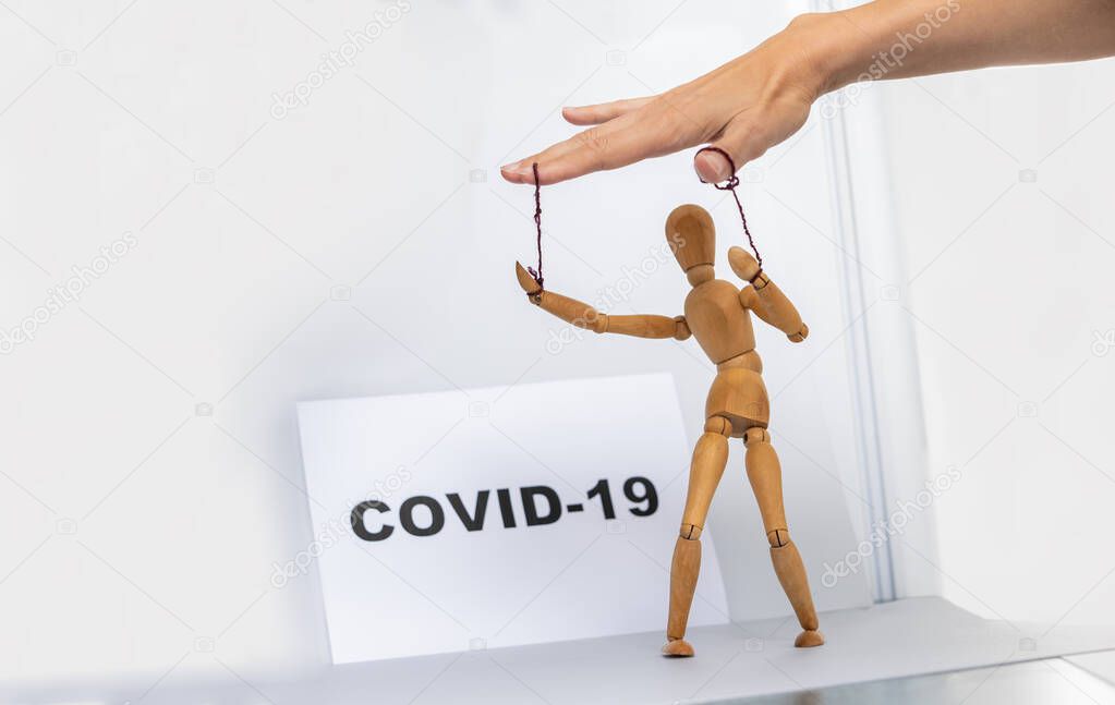 Marionette in human hand with Covid-19 inscription in the background
