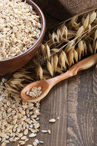 Oatmeal in a clay bowl, stalks of oats on the background of wood — Stock Photo, Image