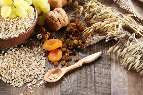 Oatmeal in a clay bowl, stalks of oats, dried apricots, raisins, — Stock Photo, Image