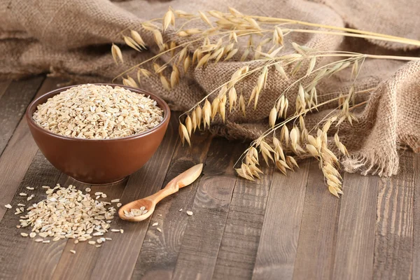 Harina de avena en un tazón de barro, tallos de avena sobre el fondo de madera —  Fotos de Stock