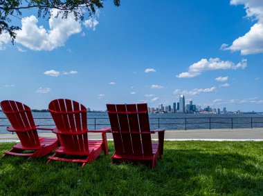Vali adasından Jersey City manzaralı üç kırmızı bahçe sandalyesi.