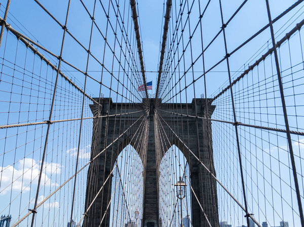 Brooklyn Bridge on bright summer day in New York with American flag waving in wind