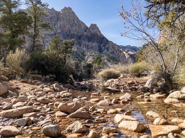 Las Vegas, Nevada 'daki Red Rock Kanyonu' nun arka planında kırmızı çizgili dağlar olan kayaların arasından akan küçük bir dere.