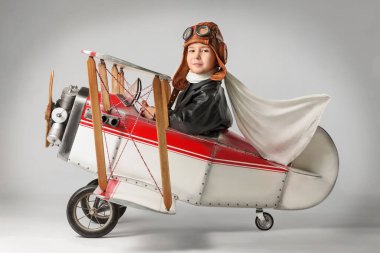 Pilot kıyafetli küçük çocuk uçakla oynuyor.