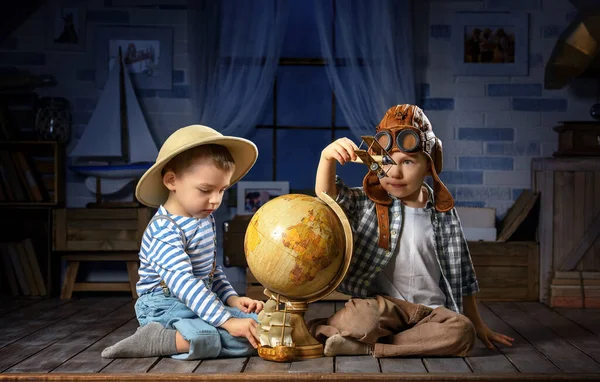 两个穿着飞机驾驶员和旅行者形象的小男孩在房间里玩地球仪 — 图库照片