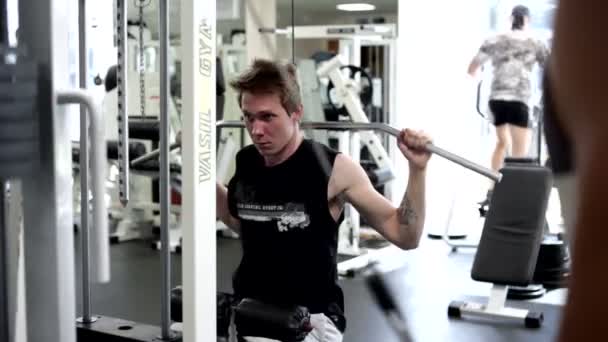 Jovem homem usa máquina de gordura (aparelho de treinamento ) — Vídeo de Stock