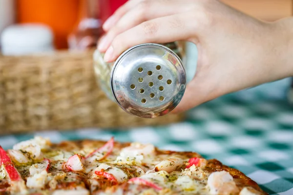 Spreading oregano spices in to pan of pizza