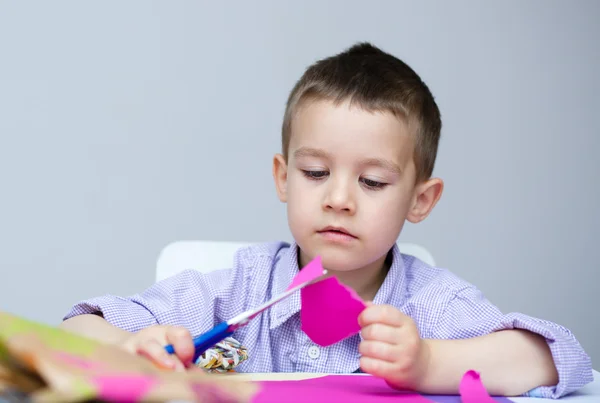 Boy is cutting paper using scissors — Stock Photo, Image