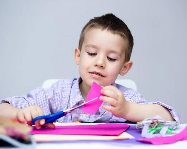 Boy is cutting paper using scissors — Stock Photo, Image