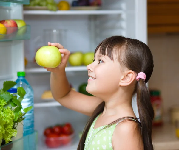 冷蔵庫近く幸せな女の子食用リンゴに立っています。 — ストック写真