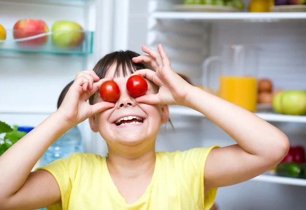 Chica comiendo tomates de pie cerca del refrigerador — Foto de Stock