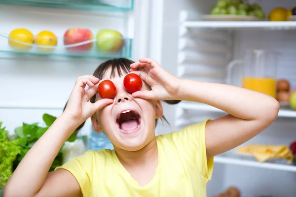 Chica comiendo tomates de pie cerca del refrigerador — Foto de Stock
