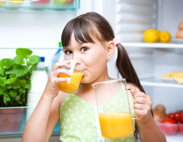 Dziewczyna pić sok pomarańczowy stojący w pobliżu lodówka — Zdjęcie stockowe