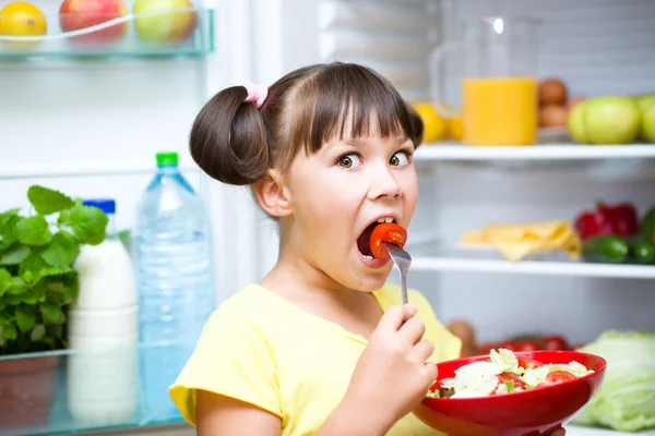 Дівчина їсть салат, стоячи біля холодильника — стокове фото