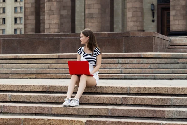 Young woman with laptop sitting on stairs near the university — Stock Photo, Image