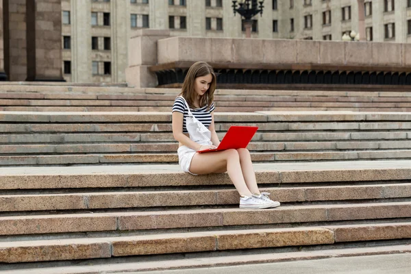 Young woman with laptop sitting on stairs near the university — Stock Photo, Image