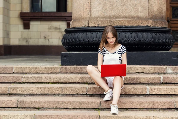 Young woman with laptop sitting on stairs near the university — Stock Photo, Image