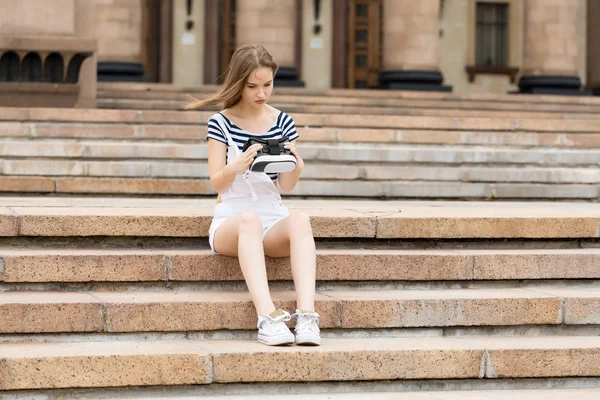 Young girl sitting on the stairs, near the university, is in virtual reality, in VR — Stock Photo, Image