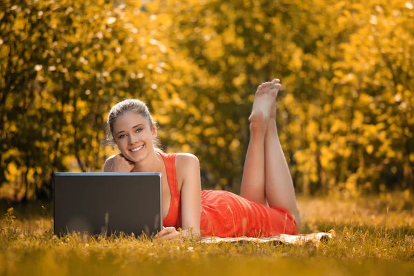 Jonge vrouw met laptop in het park op gras, in de herfst — Stockfoto