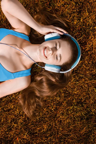 Jeune femme avec écouteurs écoutant de la musique dans le parc sur l'herbe, en automne — Photo