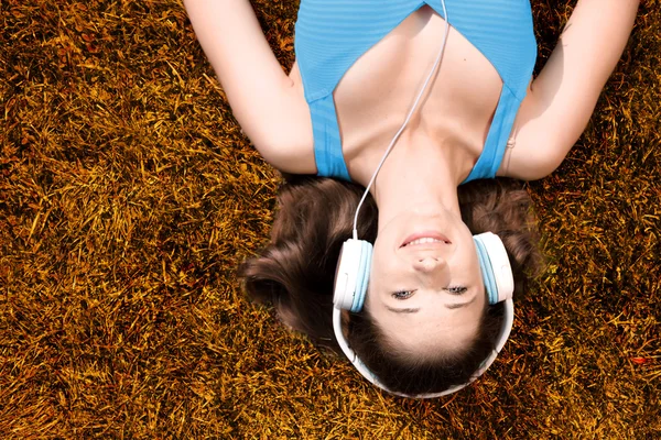 Jeune femme avec écouteurs écoutant de la musique dans le parc sur l'herbe, en automne — Photo