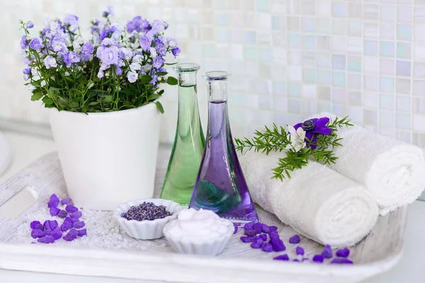 Still life, massage oil in bottles, with flowers, on a tray towels and herbs in the spa. — Stock Photo, Image