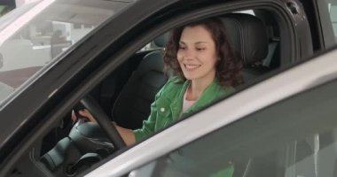 Genç ve güzel bir kız araba galerisinde yeni bir araba seçiyor. Kadın mutlu, gülümsüyor ve yeni bir araba almaktan zevk alıyor. Yeni bir araca saygı duyan bir kız. Alıcı katalogdan bir araba seçer