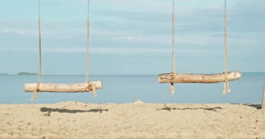 Deniz kıyısında, okyanusta sallan. El yapımı ahşap salıncaklar, şafak vakti baraj gölünün kıyısında insanlar olmadan. Kumlu sahilde el işi sallama. Salıncakta sallanmak