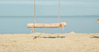 Deniz kıyısında, okyanusta sallan. El yapımı ahşap salıncaklar, şafak vakti baraj gölünün kıyısında insanlar olmadan. Kumlu sahilde el işi sallama. Salıncakta sallanmak